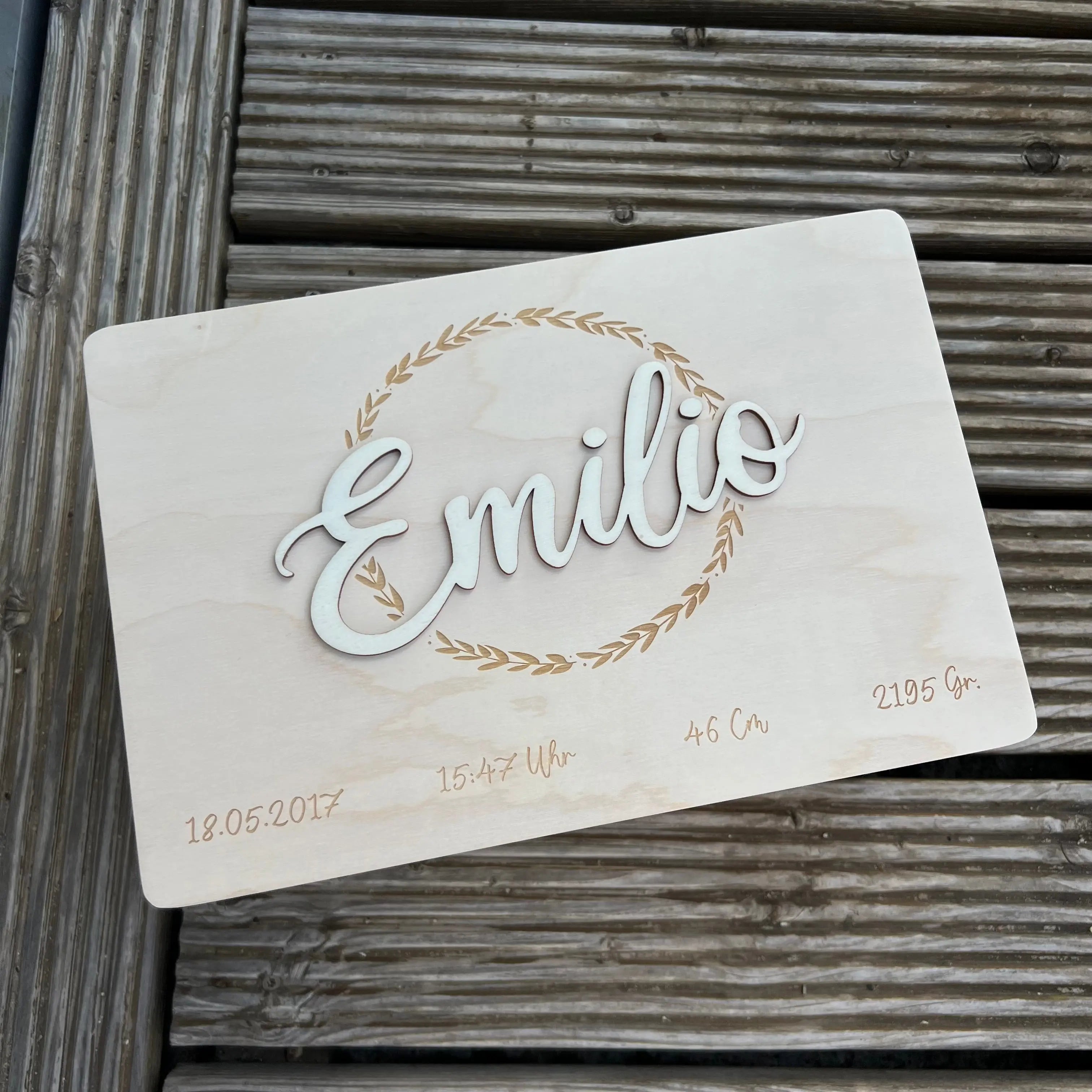Personalisierte Holztafel mit dem Namen Emilio im 3D-Schriftzug, umrahmt von einem Blätterkranz